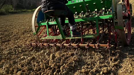 sowing-in-the-field-with-traditional-green-seeder,-following-close-up-shot