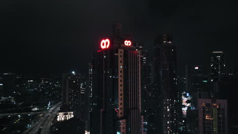 Drone-rising-around-the-illuminated-AM-bank-tower,-night-in-Kuala-Lumpur,-Malaysia