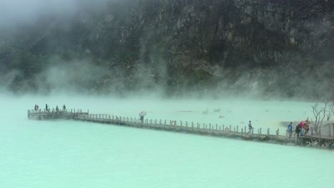 tourists-walking-on-a-bridge-in-Kawah-Putih-sulfur-lake-in-Bandung-Indonesia,-aerial