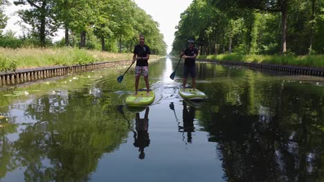 Dos-Hermanos-Pedaleando-Por-El-Canal-Con-Una-Tabla-De-Surf-De-Remo