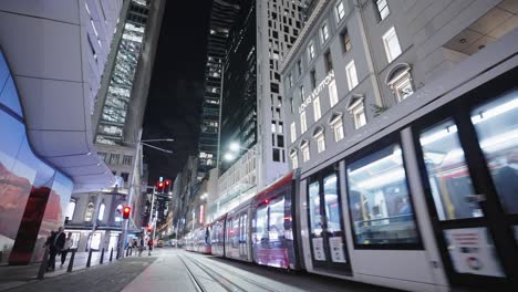 Tram-passing-through-modern-city-at-night,-George-Street,-Sydney,-Australia