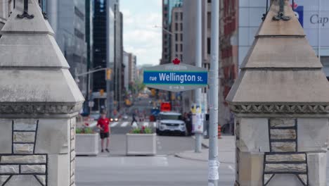 Wellington-Street-sign-on-Parliament-Hill,-Ottawa-before-Canada-Day-2022-on-a-sunny-summer-day-with-a-tour-bus-passing-in-the-background---4K-slow-motion