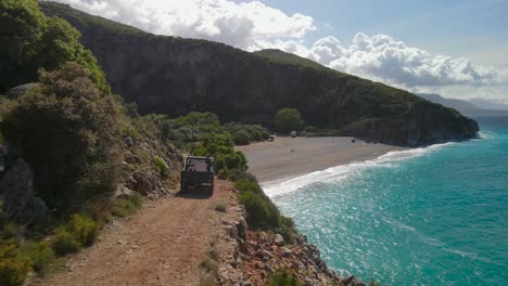 Car-driving-along-unpaved-coastal-road,-Gjipe-Beach,-Ionian-Sea,-Vlorë-County,-Albania