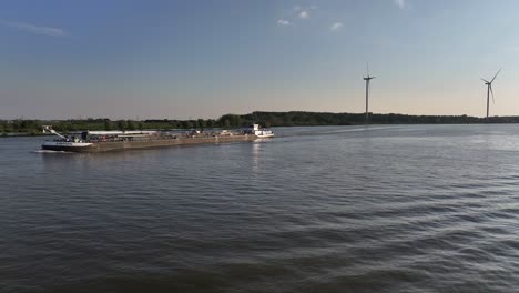 Tanker-ship-Lotus-on-river-by-wind-turbines-in-Netherlands,-wide-aerial