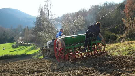 Personas-Sembrando-El-Campo-De-Tierra-Con-Tractor-De-Orugas-Y-Sembradora-Al-Atardecer,-Contraluz-De-Humo-Diésel,-Toma-Cercana