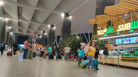 30-04-2022-Foodcourt-with-people-standing-waiting-in-line-for-Subway-sandwich-store-and-passengers-passing-in-Bangalore-airport