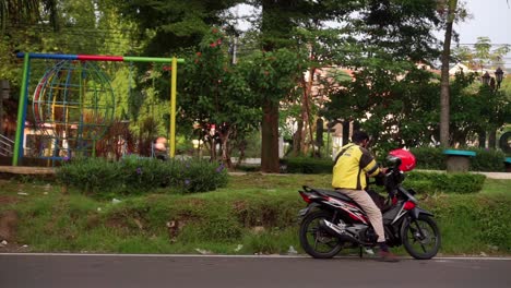 Un-Hombre-Con-Una-Chaqueta-De-Conductor-&quot;Maxim&quot;-Se-Sienta-En-Una-Motocicleta-Junto-Al-Parque-De-La-Ciudad,-Semarang,-Java-Central,-Indonesia,-El-10-De-Junio-De-2022