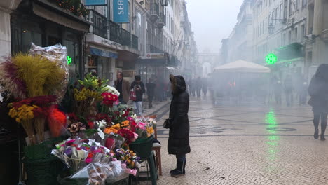 Rua-Augusta-on-a-winter-day,-with-a-lot-of-fog,-a-stall-selling-flowers-and-people-walking-around-the-city