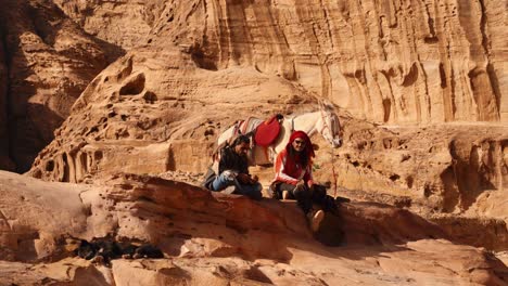 Dos-Hombres-Beduinos-Con-Un-Caballo-Sentados-En-El-Tesoro-De-Petra,-Un-Sitio-Histórico-Declarado-Patrimonio-De-La-Humanidad-Por-La-UNESCO,-Tallado-En-Piedra-Arenisca-En-Jordania