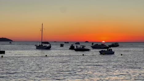 Boats-anchored-on-calm-waters-as-the-sun-sets-in-Ibiza,-Spain,-creating-a-serene-evening-scene