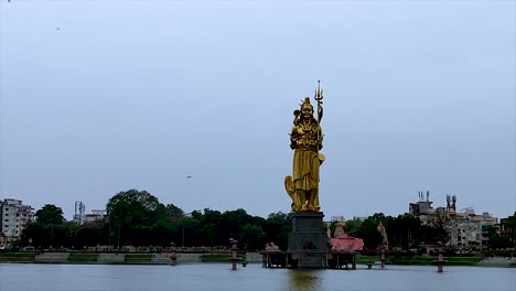 Static-shot-of-Sursagar-Lake-with-golden-Lord-Shiva's-statue,-on-cloudy-day-in-Vadodara,-Gujarat,-India