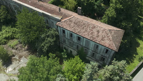 Abandoned-Italian-school-surrounded-by-overgrown-greenery,-shot-from-an-aerial-view