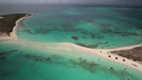 A-turquoise-sea-surrounding-a-sandy-isthmus-at-los-roques-archipelago,-aerial-view