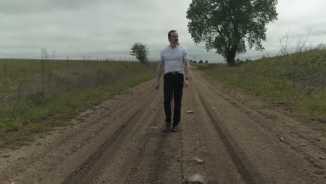 Man-walking-on-dirt-road-by-expansive-fields