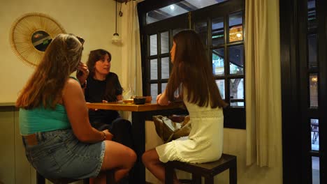 Three-women-talking-about-a-phone-conversation-in-a-cozy-cafe-setting