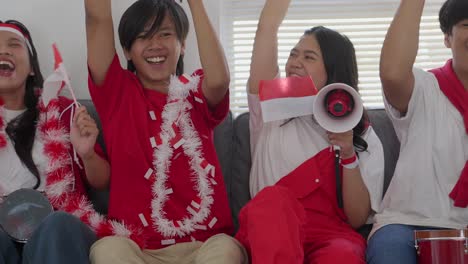 Group-Of-Young-Men-And-Women-Indonesian-Football-Supporters-Stacking-Hands,-Cheering-Using-Tamborine-and-Megaphone-Celebrates-Team-winning