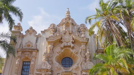 The-ornate-facade-of-Casa-del-Prado-in-Balboa-Park-exemplifies-the-baroque-architectural-style,-surrounded-by-lush-palm-trees-that-enhance-its-historical-and-cultural-significance