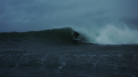 In-water-view-of-surfer-crouched-down-as-they-pop-up-from-getting-barreld-on-rainy-stormy-day,-slow-motion