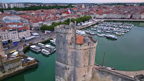 Chain-and-Saint-Nicolas-towers-with-French-flag-waving,-La-Rochelle-old-port,-France