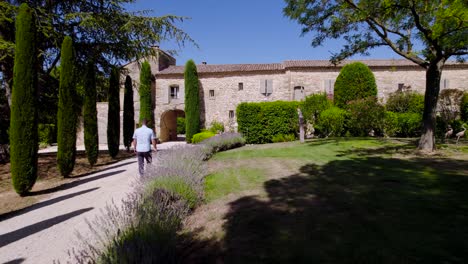 Adult-male-walking-towards-french-farmhouse-mansion-in-southern-France,-overview-property