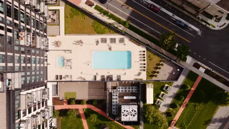 Toma-Aérea-De-Arriba-Hacia-Abajo-Con-Dron-De-Una-Piscina-Al-Aire-Libre-Junto-A-Un-Edificio-De-Condominios-De-Gran-Altura