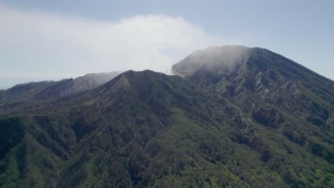 Aerial-Closeup-of-the-rim-of-a-steaming-volcano-Ijen-with-a-Turquoise-Lake,-and-foggy-cloudy-Mountain-in-the-background---East-Java,-Indonesia