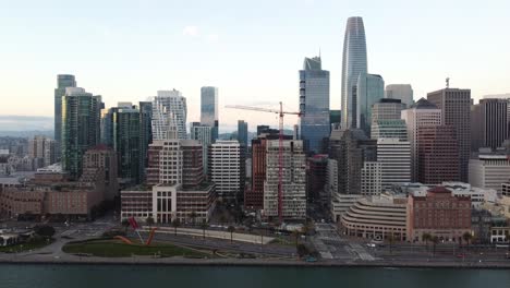 From-above,-a-drone-zooms-in-to-capture-Rincon-Park-in-San-Francisco,-highlighting-the-area's-blend-of-nature,-historic-architecture,-and-the-bustling-energy-of-the-city’s-waterfront