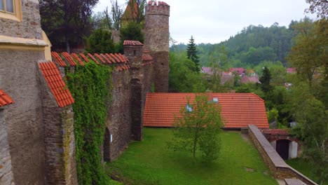 Medieval-castle-walls-with-a-tall-tower,-grey-stone,-red-tiles,-and-green-lawn