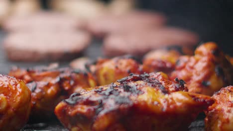 Primer-Plano-De-Muslos-De-Pollo-Crujientes-Marinados-Cocinándose-En-Una-Barbacoa-Humeante-Con-Hamburguesas-De-Fondo-Para-Una-Celebración-De-Barbacoa-Familiar-En-Cámara-Lenta-4k