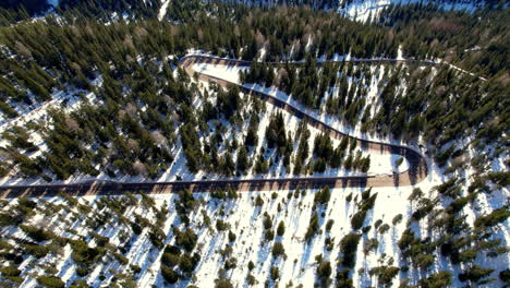 A-mesmerizing-aerial-view-of-a-winding-road-cutting-through-a-dense,-snowy-forest-in-the-Dolomites