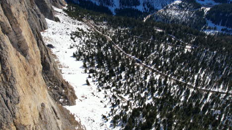 Luftaufnahmen-Einer-Steilen-Felswand-Und-Eines-Verschneiten-Waldes-In-Den-Dolomiten,-Die-Das-Zerklüftete-Gelände-Und-Die-Natürliche-Schönheit-Hervorheben