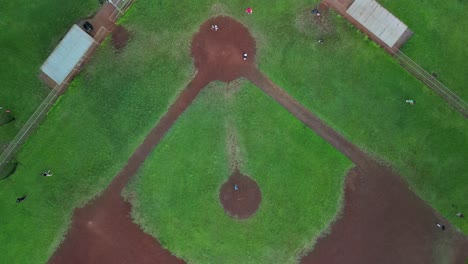 Una-Vista-Aérea-De-Niños-Jugando-Béisbol-En-Un-Campo-Verde.