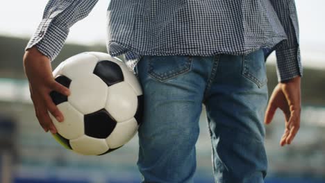 Little-boy,-child-standing-at-empty-sport-stadium-with-football-ball.-Dreaming-of-becoming-soccer-sportsman.-Concept-of-childhood,-dreams,-imagination-and-future,-sport