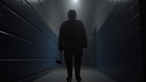 A-hockey-player-in-red-uniform-walking-down-dark-hallway-in-arena