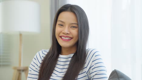 Portrait-of-Asian-beautiful-woman-sit-on-sofa-in-living-room-at-home.-Attractive-young-female-feeling-happy-and-relax-enjoy-early-morning-weekend-activity-lifestyle-in-house-and-smile,-look-at-camera.