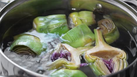 Put-and-cooking-artichokes-in-saucepan,-closeup-in-the-kitchen