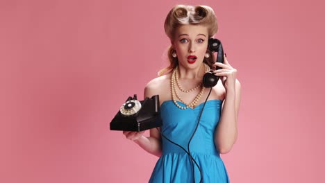 Emotional-phone-talk.-Beautiful-young-girl-with-stylish-hair-and-bright-makeup-talking-with-different-emotions-on-pink-background.-Concept-of-retro-fashion,-beauty,-attraction,-50s,-60s.-Pin-up-style