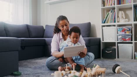 Mamá-Usa-Una-Tableta-Mientras-Está-Sentada-En-El-Suelo-Con-Un-Niño