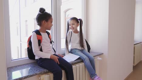 Two-cheerful-children-sitting-on-windowsill-and-laughing