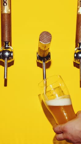 Bartender-slowly-pouring-delicious-lager-foamy-beer-against-yellow-background.-Bubbles.-Beer-bar,-degustation.-Concept-of-brewery,-taste,-bar,-degustation,-festival,-drink-texture.-Vertical-layout