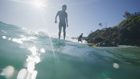 Dos-Surfistas-Surfeando-En-Una-Sola-Ola-En-Aguas-Cristalinas-En-Byron-Bay,-Australia,-Filmados-Desde-El-Agua-En-Cámara-Lenta