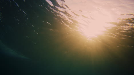 Glowing-orange-golden-light-sparkles-across-underwater-breaking-wave-with-surfer