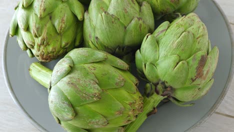 Whole-fresh-artichokes-on-plate,-rotate.-Closeup