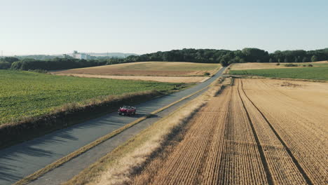 An-aerial-view-of-a-red-vintage-convertible-car-driving-through-agricultural-fields-in-Germany