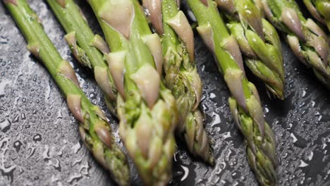 Raw-green-asparagus-on-wet-black-slate-background.-Rotating