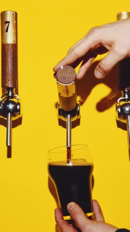 Bartender-slowly-pouring-delicious-dark-beer-in-glass-against-yellow-background.-Bubbles.-Beer-bar,-degustation.-Concept-of-brewery,-taste,-bar,-degustation,-festival,-drink-texture.-Vertical-layout