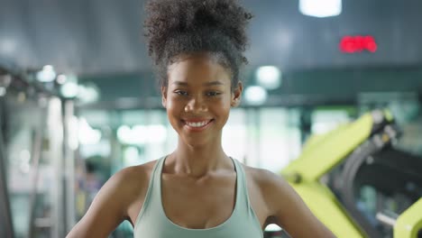 Portrait-of-African-sport-girl-in-sportwear-exercising-in-fitness-club.-Attractive-athlete-young-female-stand-and-crossing-arms-after-finish-workout-with-machines-and-equipment-in-gym-or-fitness-club.