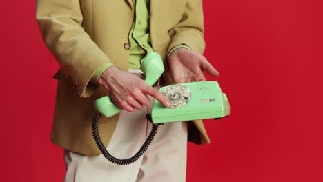 Man,-businessman-in-olive-color-jacket-dialing-a-phone-number-on-a-vintage-telephone-over-red-background.-Retro-style.-Concept-of-emotions,-business,-occupation,-facial-expression,-fashion