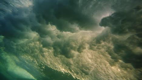 Underwater-view-of-breaking-wave-lighting-up-with-sun-rays-glowing-and-surfer