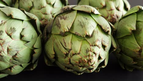 Whole-fresh-artichokes-on-black-table,-closeup